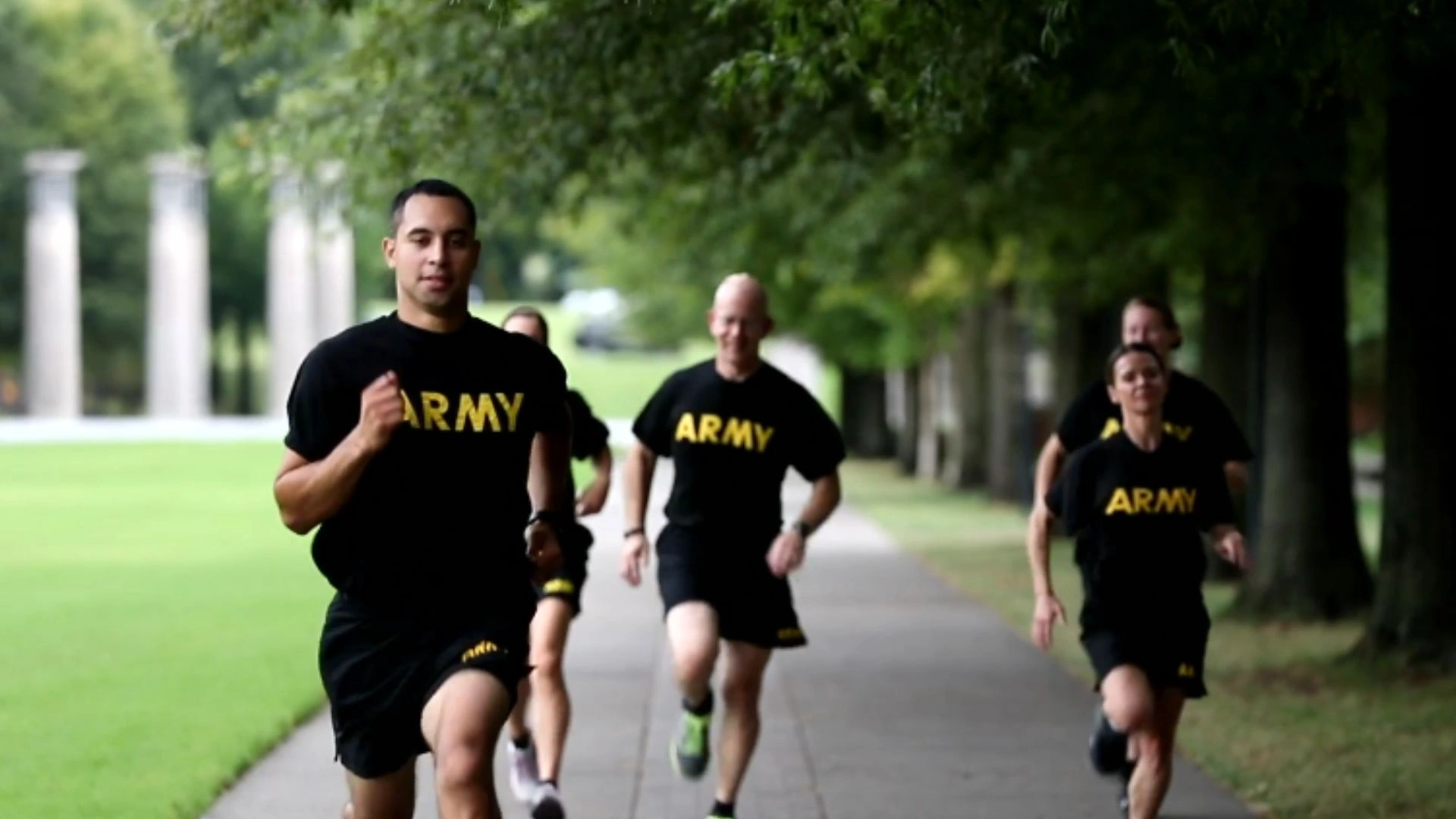 U.S. Army soldiers jogging on a tree-lined path wearing black “ARMY” shirts during the Two-Mile Run (2MR) ACFT event.