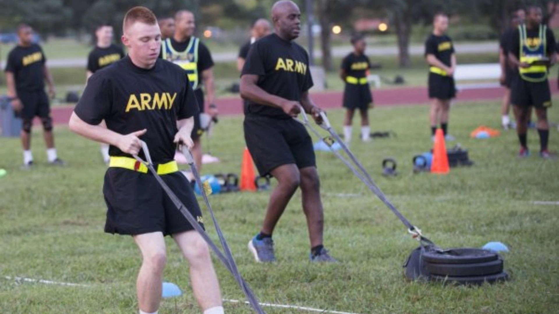 Two U.S. Army soldiers dragging sleds on grass during the SDC ACFT event