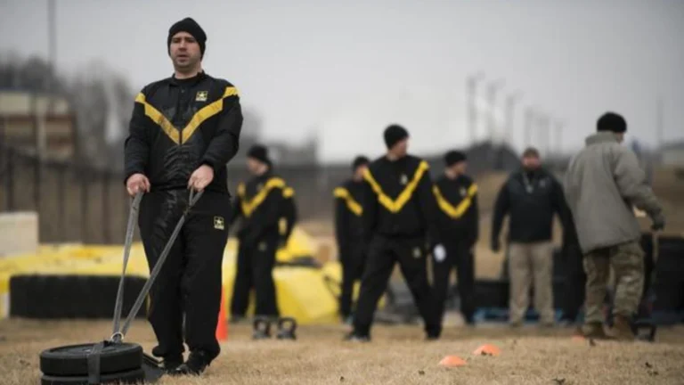 ACFT Calculator | Calculate Your Army Combat Fitness Test Score 2 Military personnel pulling a sled on a grassy field during Sprint-Drag-Carry (SDC) with others in the background